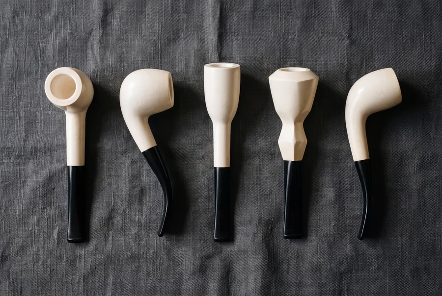Five meerschaum pipes in different classic silhouettes laid out in a row on grey linen, shown in profile